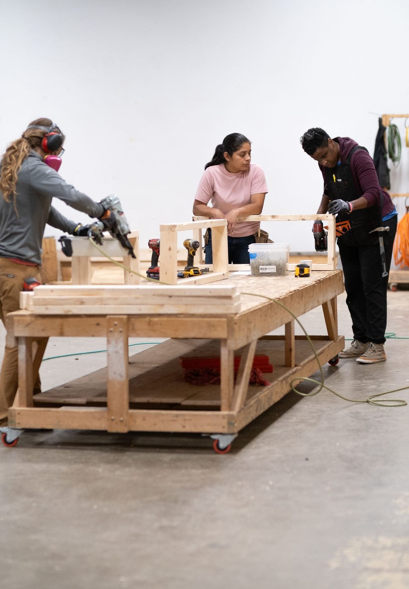 Three people at a shop workbench assembling timber panel frames