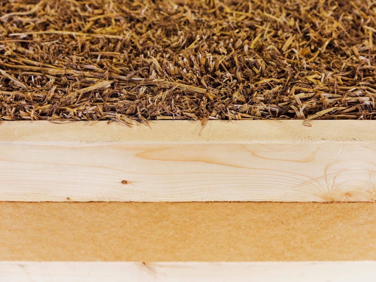 Close view of a panel edge: dense straw against a timber stud and a wood fiber board